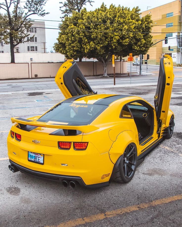 a yellow sports car with its doors open sitting in the middle of a parking lot