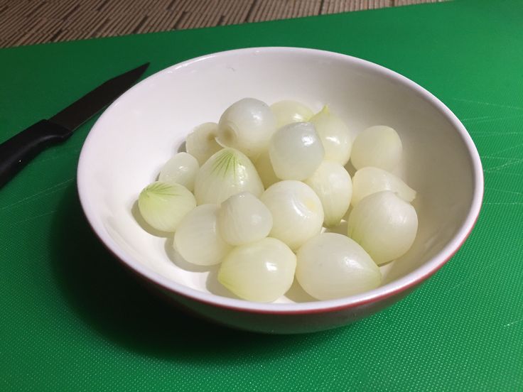 a white bowl filled with onions next to a pair of black scissors on a green place mat