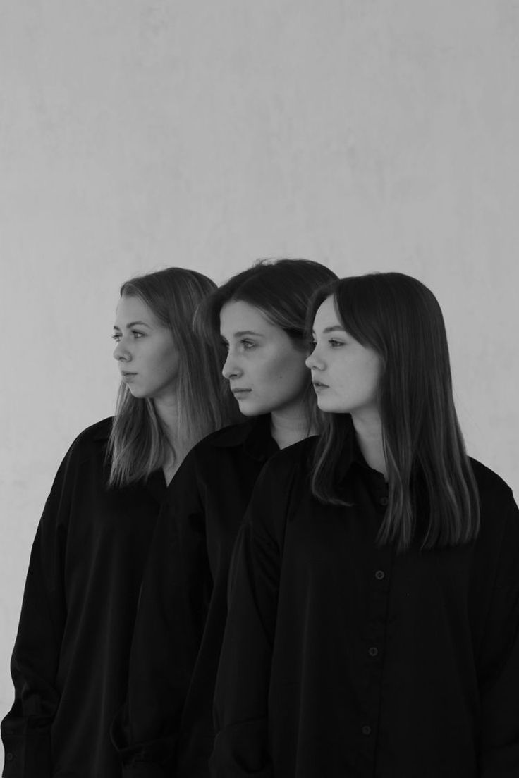 three women standing in front of a white wall with their heads turned to the side