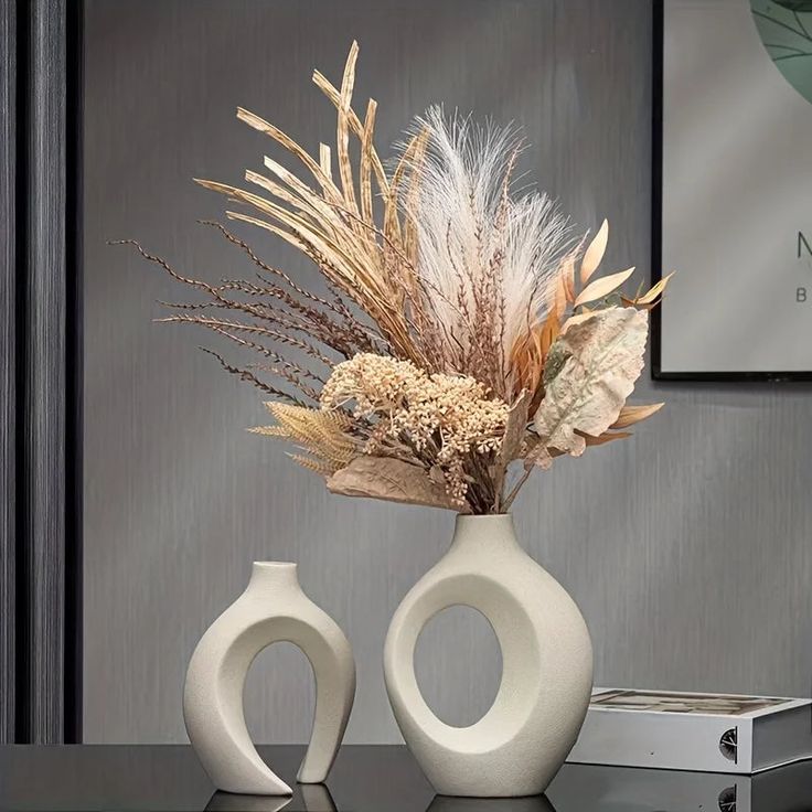 two white vases sitting on top of a table with dried flowers in them,