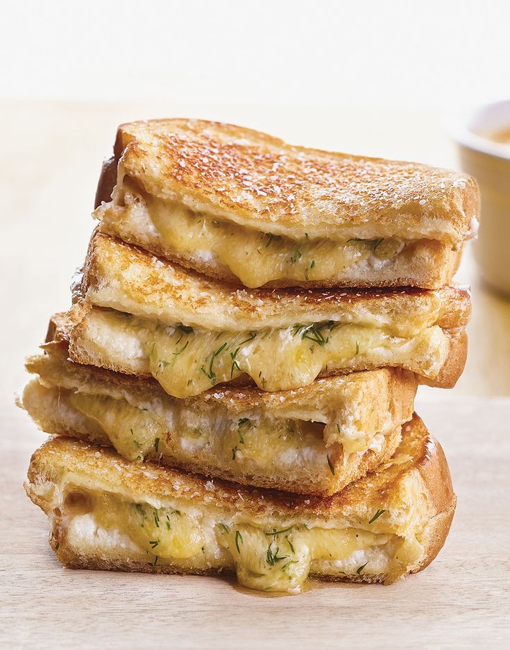 a stack of four grilled cheese sandwiches sitting on top of a wooden cutting board