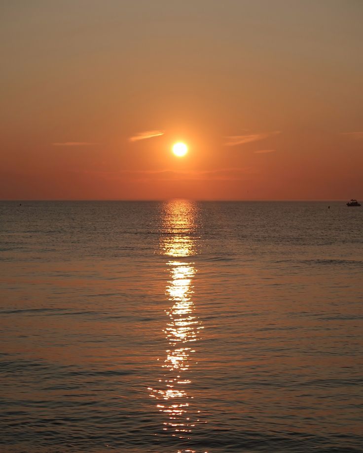 the sun is setting over the ocean with small boats in the water and one boat on the horizon