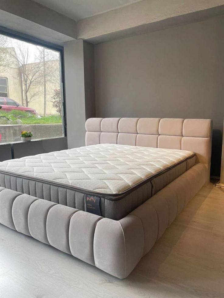 a bed sitting in the middle of a room next to a window with large windows