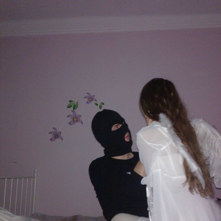 a person in a black mask sitting on a bed next to another person wearing a white dress