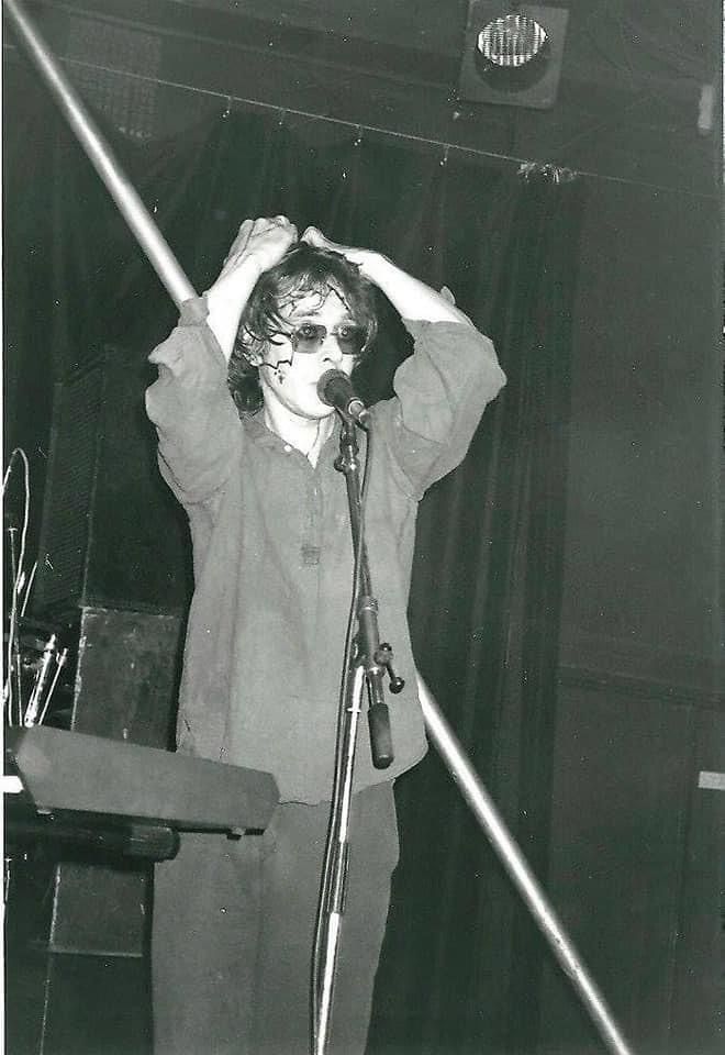 a man standing in front of a microphone on stage with his hands behind his head