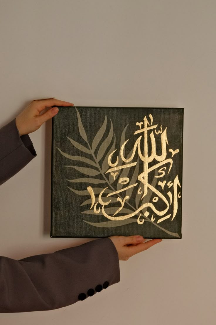 a person holding up a piece of art with arabic writing on it