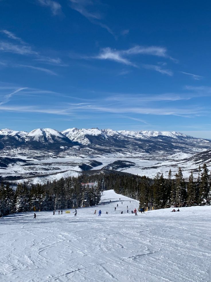 skiers and snowboarders at the top of a ski slope with mountains in the background