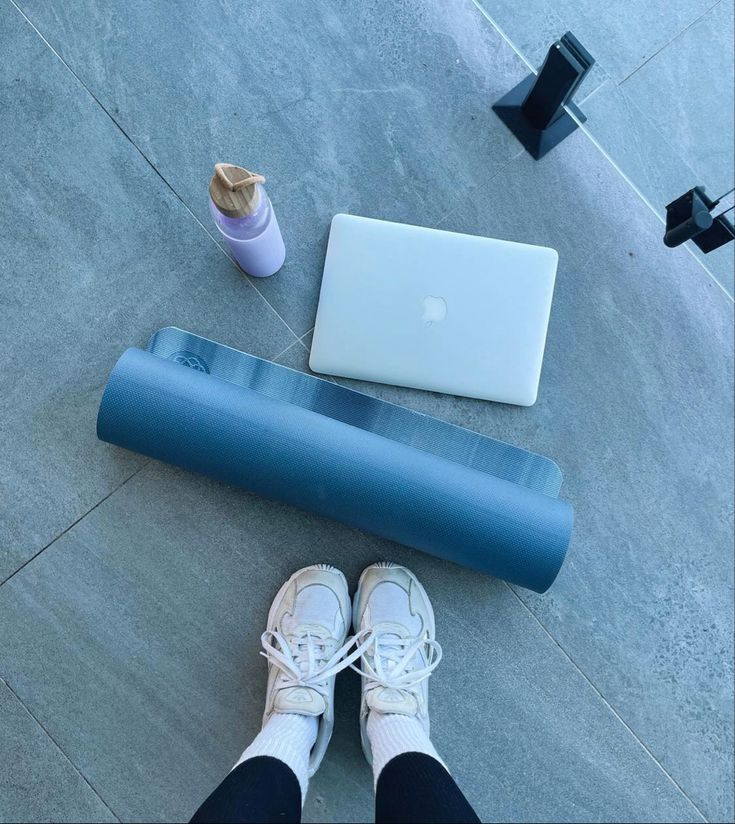 a person sitting on the ground with their feet up next to an exercise mat and laptop