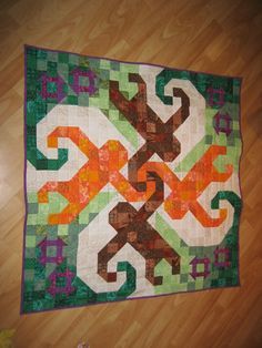 a multicolored quilt on the floor with an orange, green and brown design