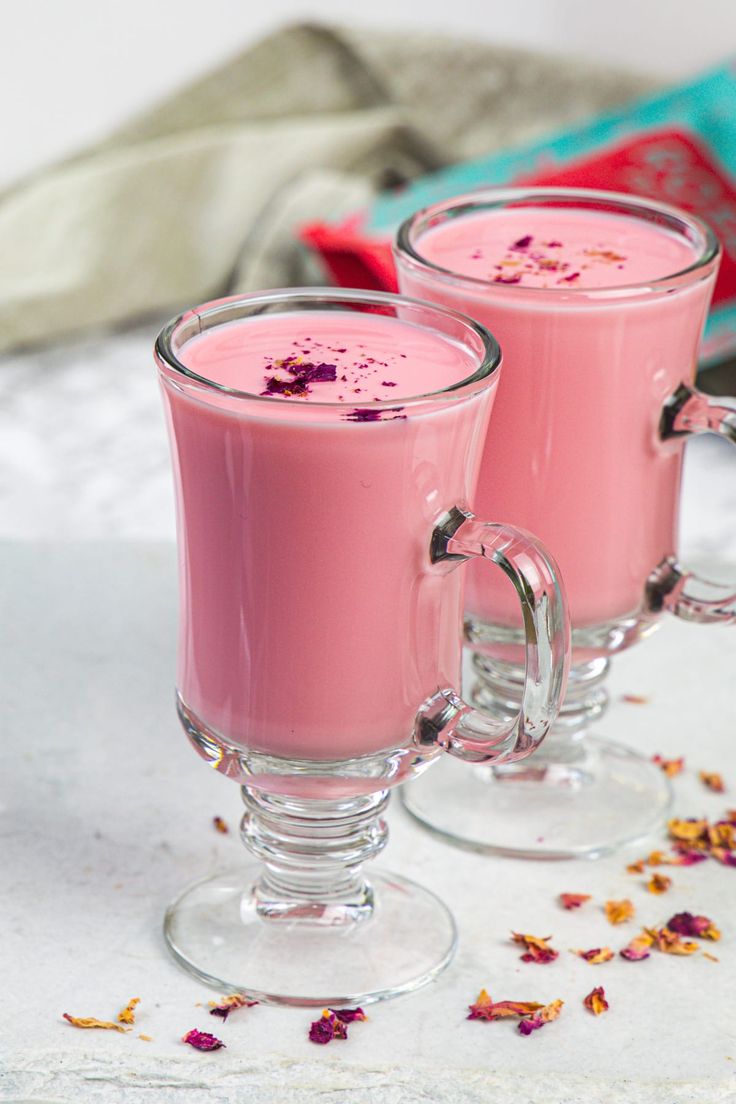 two glasses filled with pink liquid sitting on top of a white table next to a book