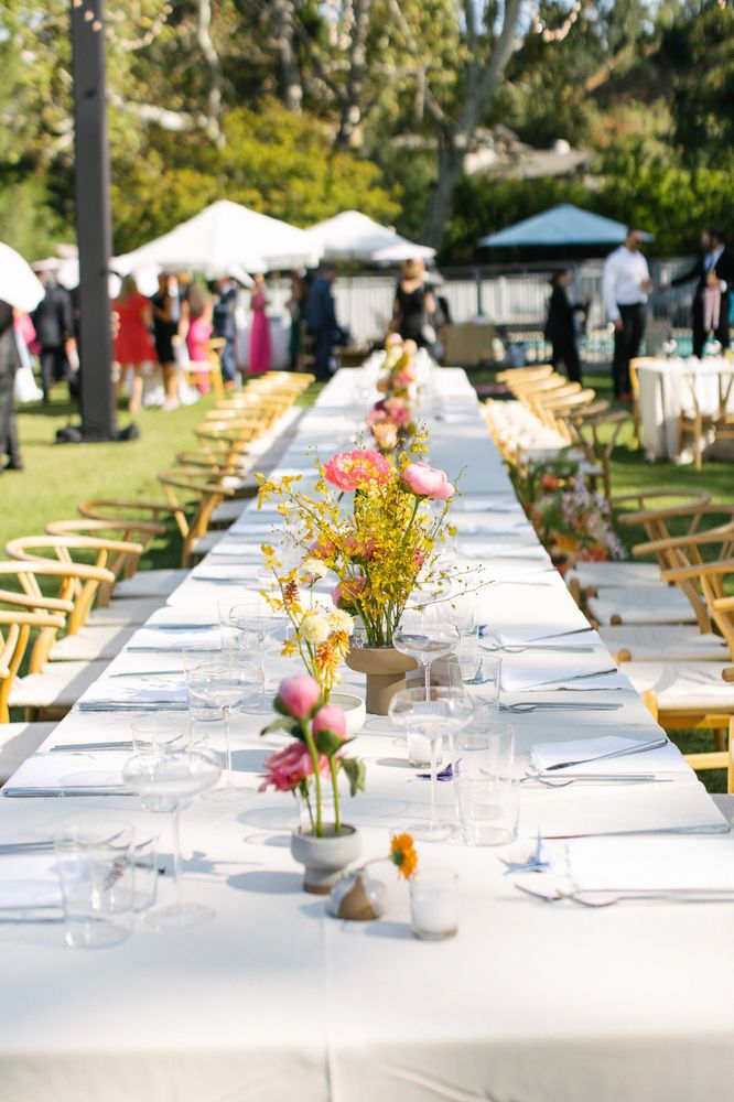 a long table is set up for an outdoor event with flowers in vases on it