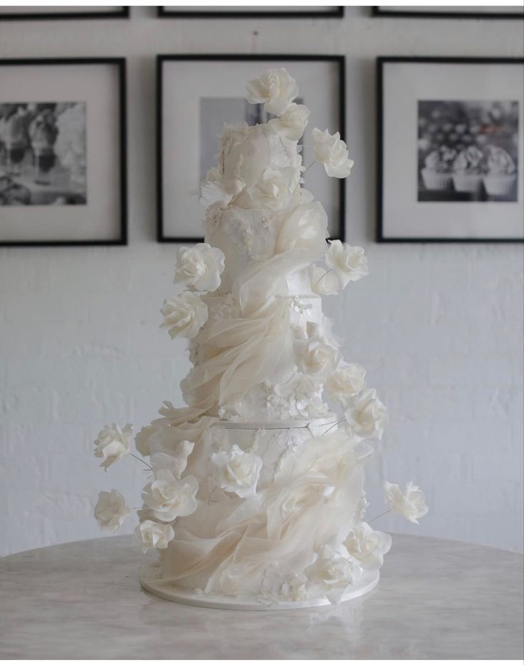 a white wedding cake with flowers on it sitting on a table in front of three framed pictures