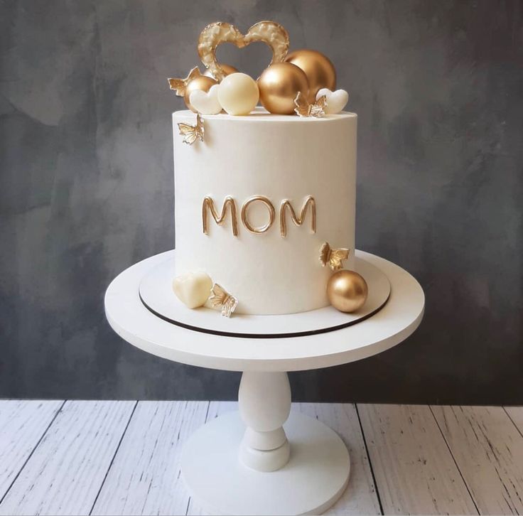 a white cake with gold decorations and the word mom on top is sitting on a pedestal