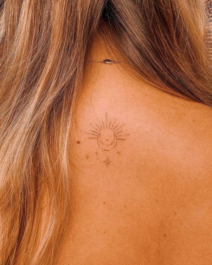 the back of a woman's neck with a small sun tattoo on her left shoulder