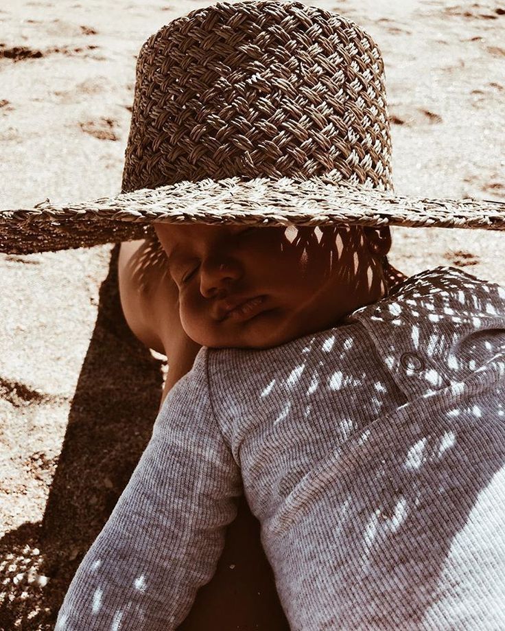 a young child wearing a straw hat laying on the ground with his head resting on someone's shoulder