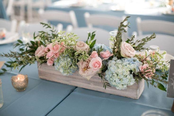 an arrangement of flowers in a wooden box on a table with candles and napkins