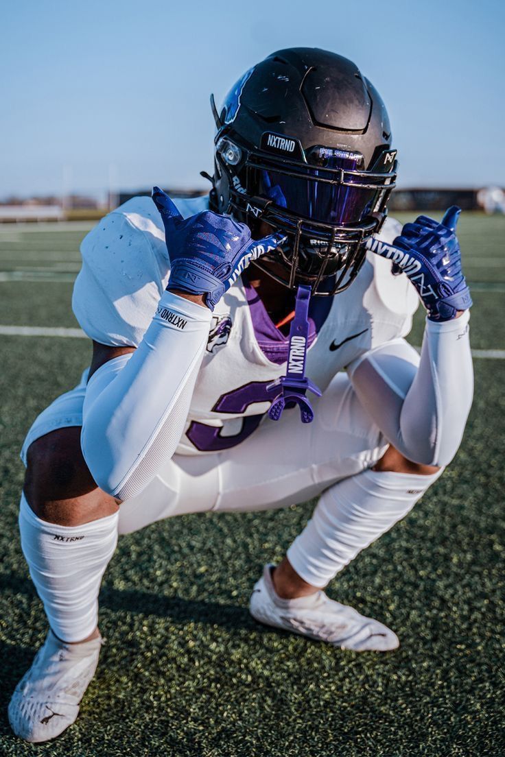 a football player kneeling down on the field with his hands in his pockets and wearing a helmet