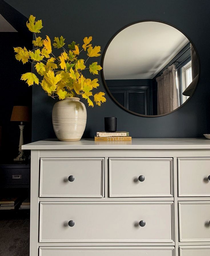 a white dresser with yellow flowers and a round mirror