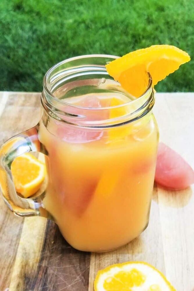 a pitcher filled with liquid sitting on top of a wooden table next to sliced oranges