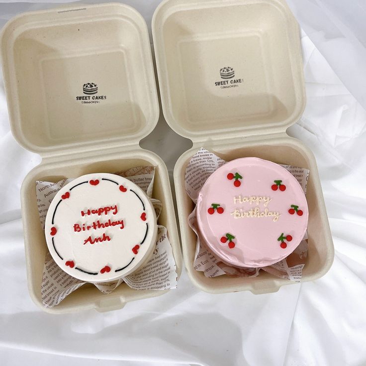 three birthday cakes in plastic containers on a bed