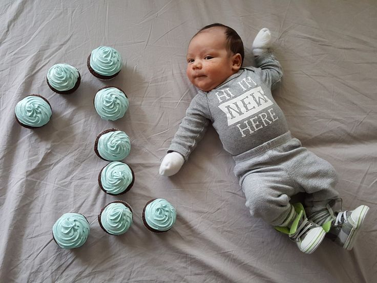 a baby laying next to some cupcakes on a sheet with frosted icing