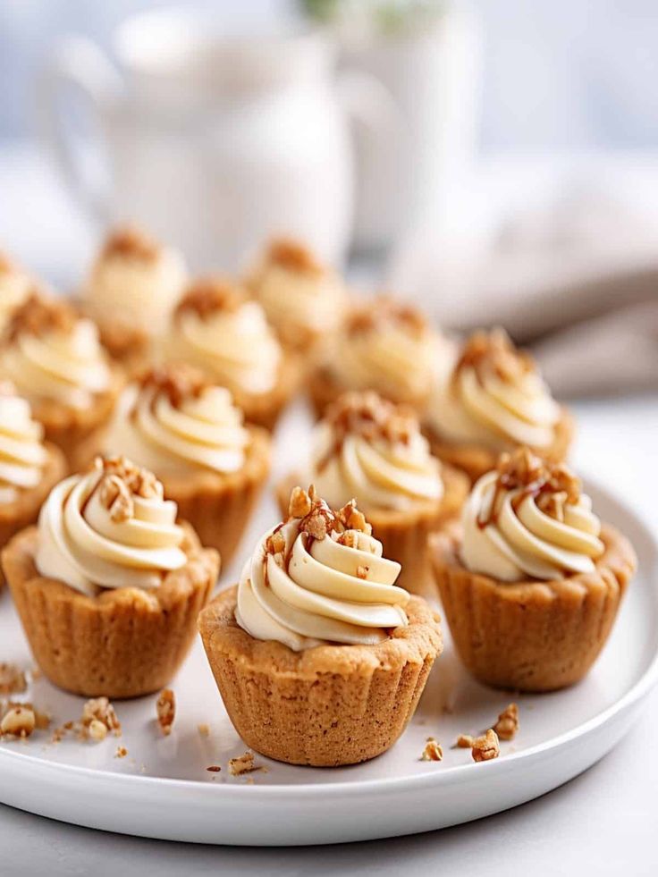 small cupcakes with white frosting and pecans scattered around them on a plate