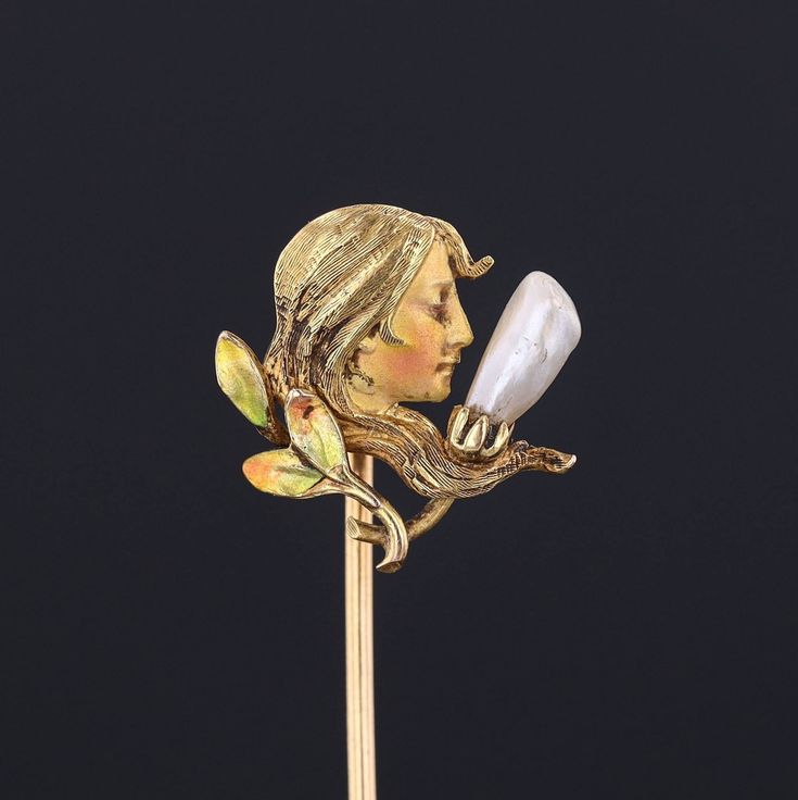 During the turn of the nineteenth century, artisans working in the Art Nouveau style were inspired by the changing roles of women in society and began depicting the free flowing feminine form in brooches, bracelets, rings and more. This antique stick pin (circa 1910-1920) features a woman of 14k gold decked out in enamel and accented with a single pearl. The piece bears the makers mark for the renowned Krementz and Co. The pin head measures 0.6 inches by 0.6 inches and 2.4 inches long. The piece Yellow Gold Enamel Brooches, Art Nouveau Jewelry With Historical Design For Formal Occasions, Art Nouveau Jewelry With Historical Design For Formal Events, Baroque Yellow Gold Brooch For Gift, Art Nouveau Historical Jewelry For Formal Occasions, Yellow Gold Baroque Brooch For Gift, Yellow Gold Baroque Brooches As Gift, Art Nouveau Yellow Gold Collectible Brooches, Art Nouveau Enamel Brooch Jewelry