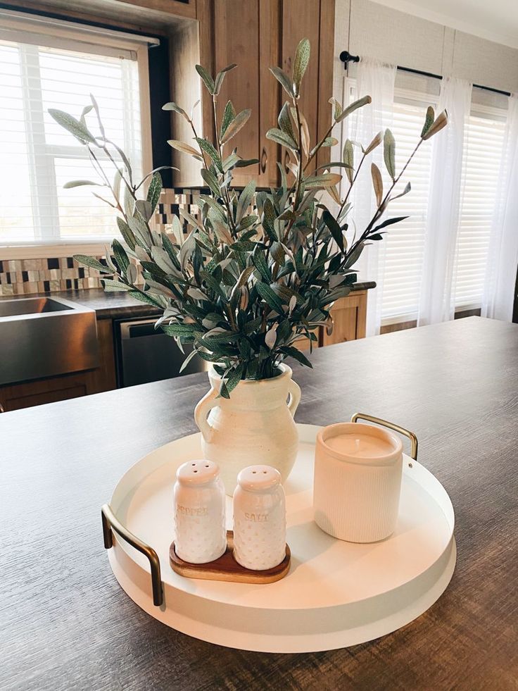 a white vase sitting on top of a wooden table next to two cups and a candle