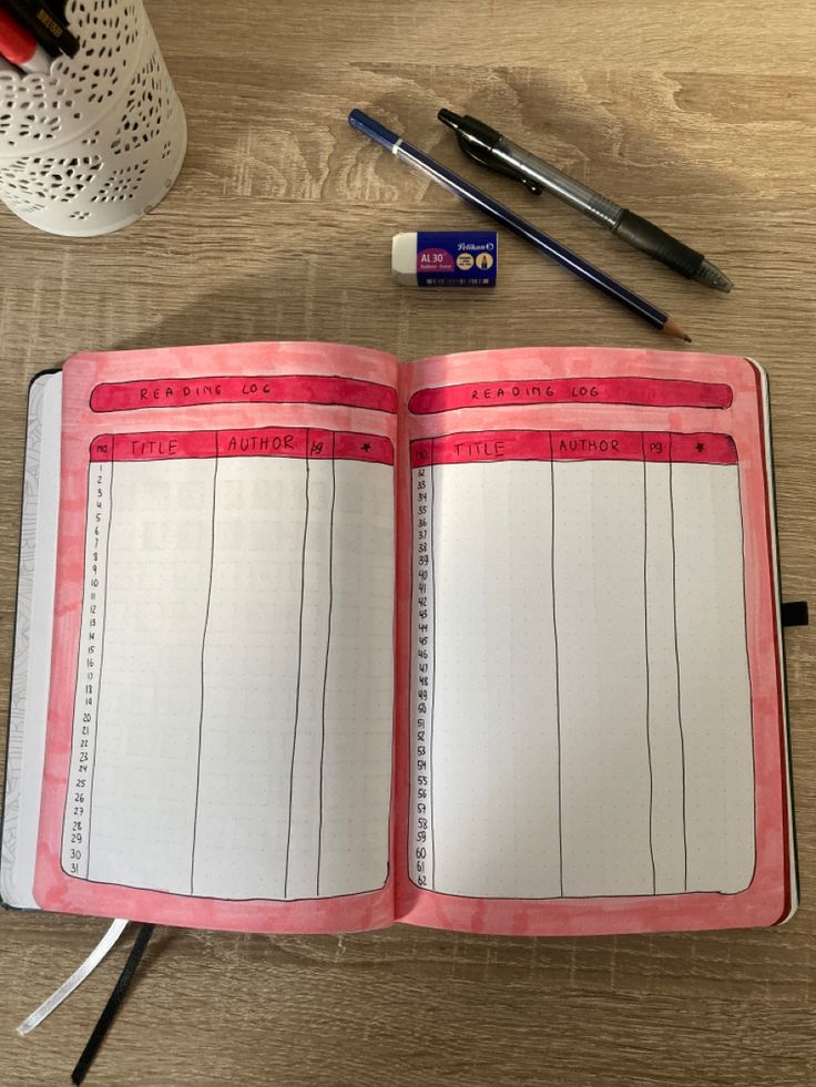 an open notebook sitting on top of a wooden table next to pens and pencils