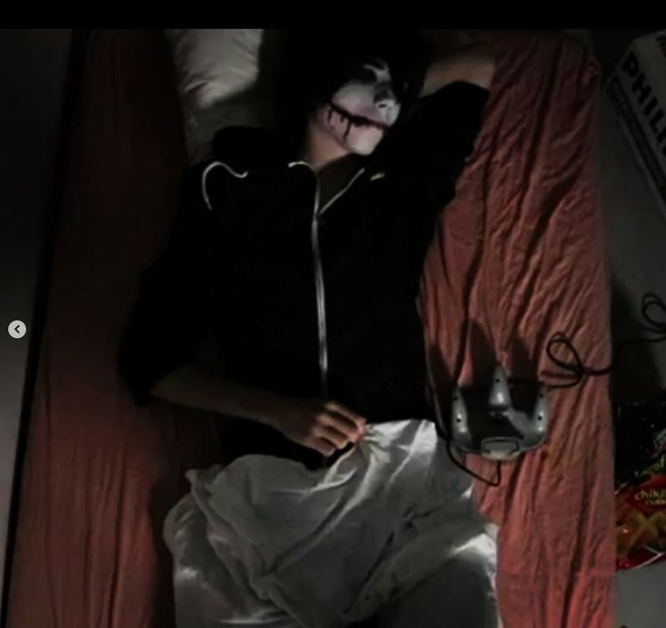 a person laying on a bed wearing a mask and holding a remote control in their hand