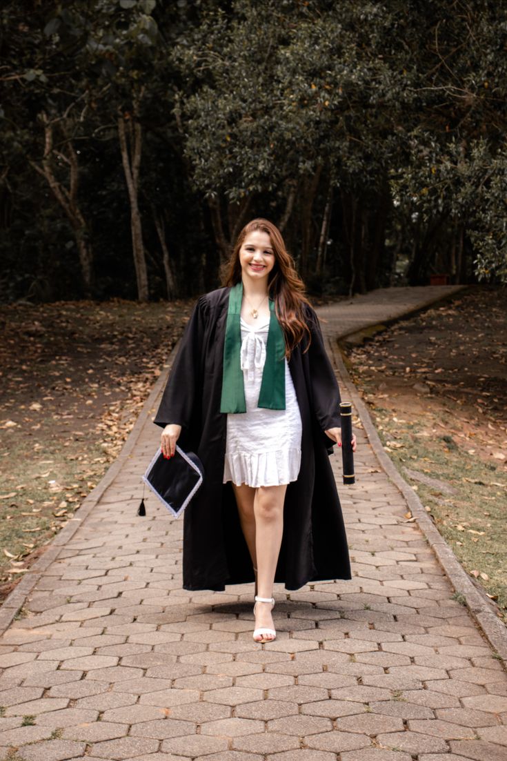 a woman walking down a brick path in a white dress and black coat with green trim