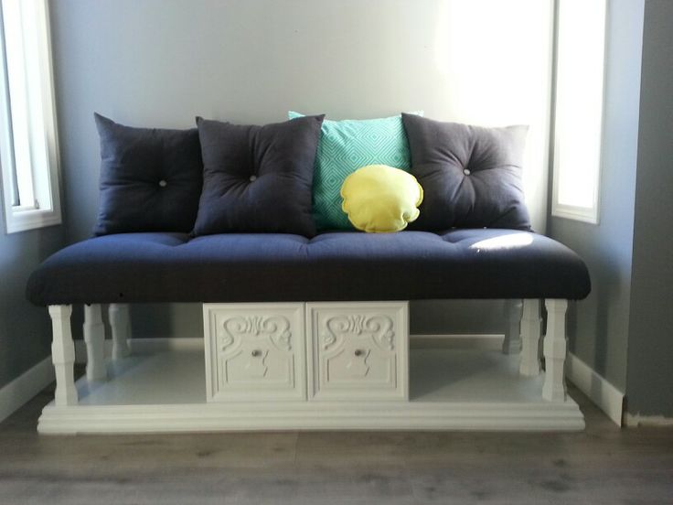 a white bench with pillows on top of it in front of a blue wall and window