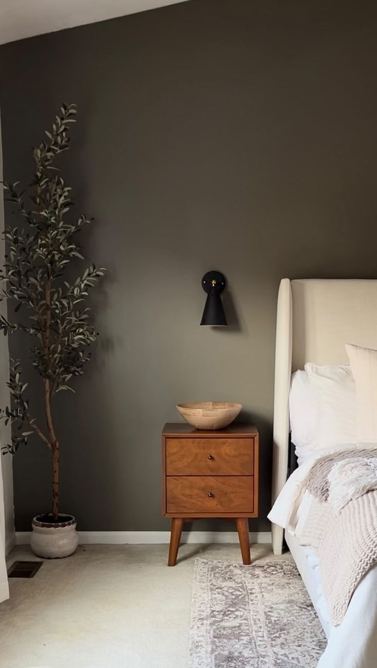 a white bed sitting next to a wooden night stand on top of a carpeted floor