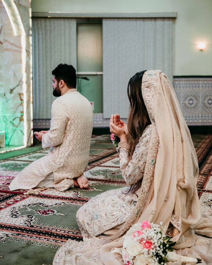 two people are sitting on the floor in their wedding outfits and one person is wearing a veil