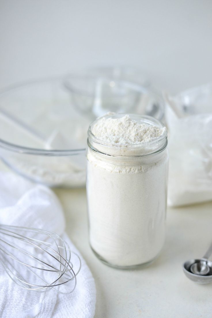 a glass jar filled with white powder next to a whisk and measuring spoon