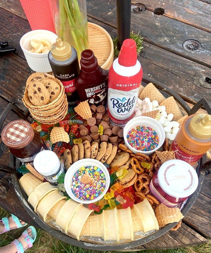 an assortment of snacks and condiments are arranged in a bowl on a picnic table