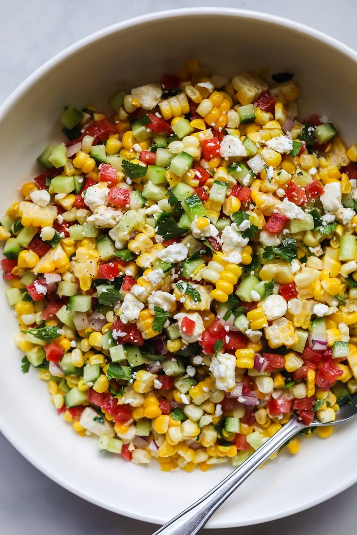 a white bowl filled with corn salad next to a fork