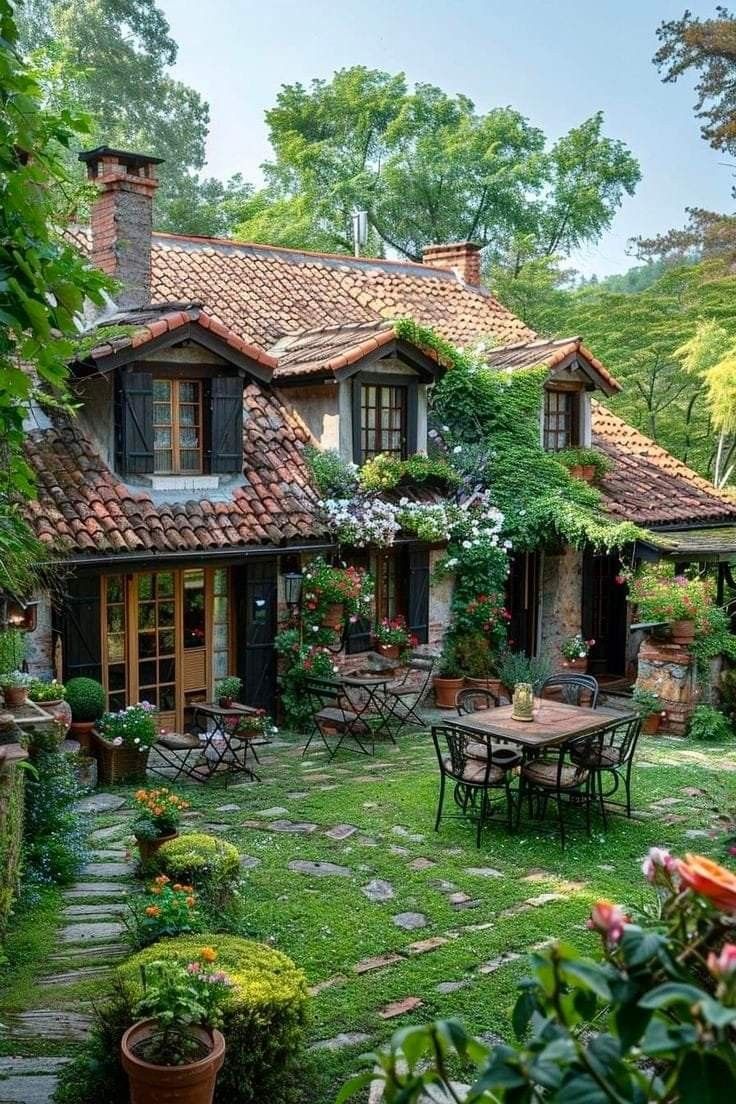 an outdoor patio with tables and chairs in front of a house surrounded by greenery