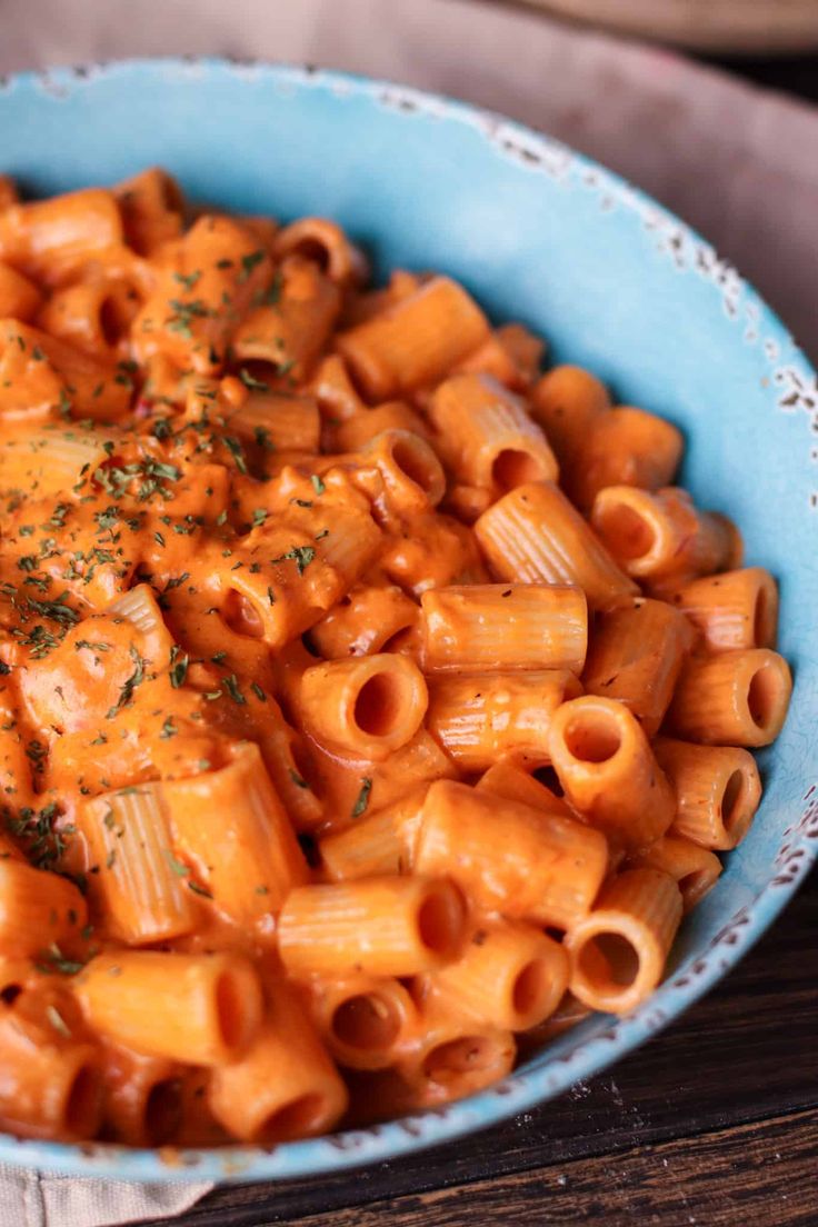 a blue bowl filled with macaroni and cheese on top of a wooden table