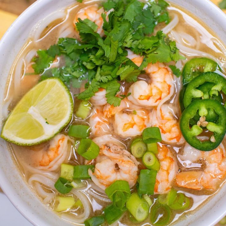 a white bowl filled with shrimp and veggies next to a slice of lime