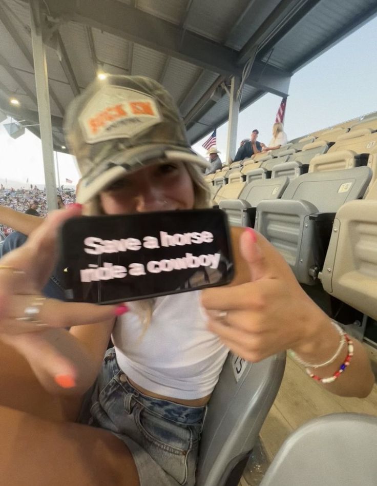 a woman sitting in a stadium holding up a cell phone