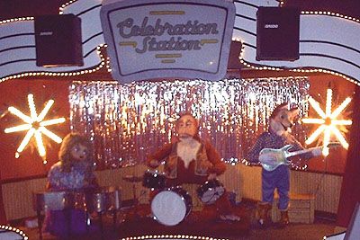 the band is performing on stage with lights in the background and people standing around playing instruments