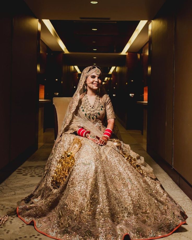 a woman sitting in a chair wearing a gold and red bridal gown with matching jewelry