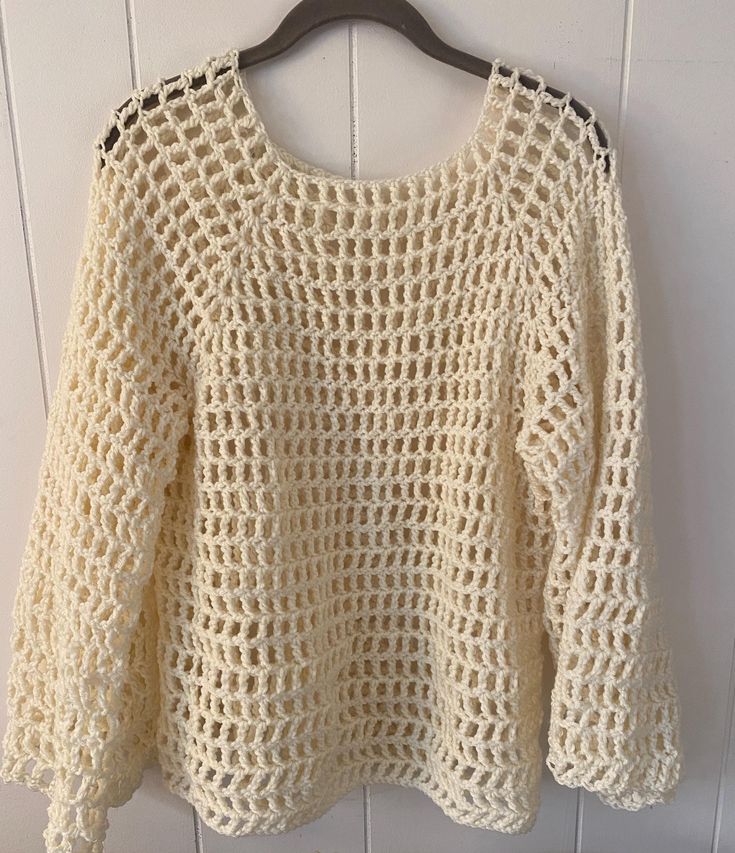 a crocheted sweater hanging on a wooden hanger