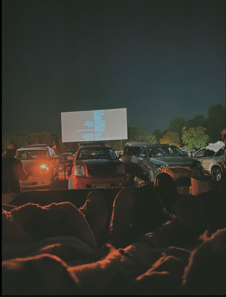 cars are parked in a parking lot at night with a projector screen above them