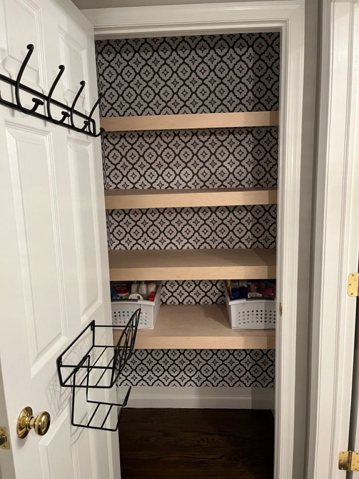 an empty pantry with shelves and baskets on the door handle, in front of a wallpapered background