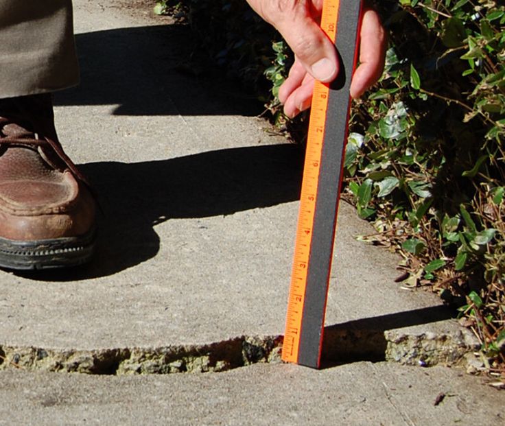 a person holding a measuring tape in their hand and standing on the sidewalk next to shrubbery