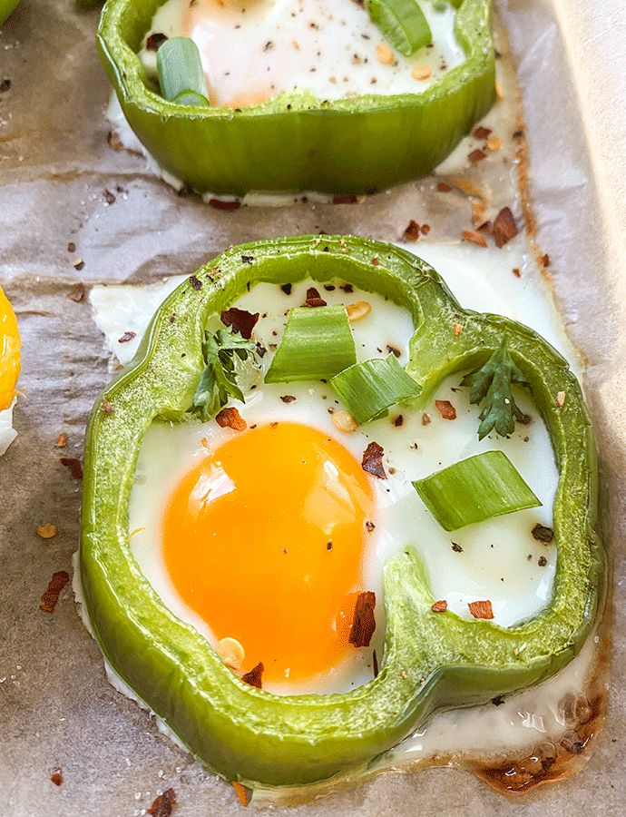 two green peppers with an egg in the middle and some other food items on top