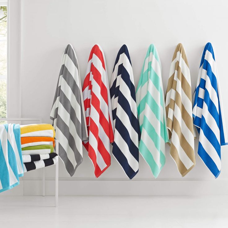 towels hanging up on a rack in a room with white walls and windows, all lined up against the wall