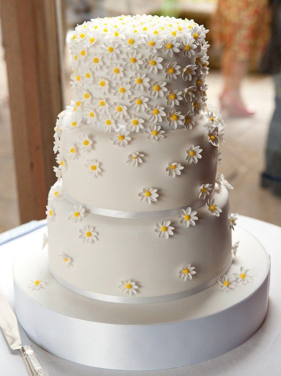 a three tiered cake with daisies on it